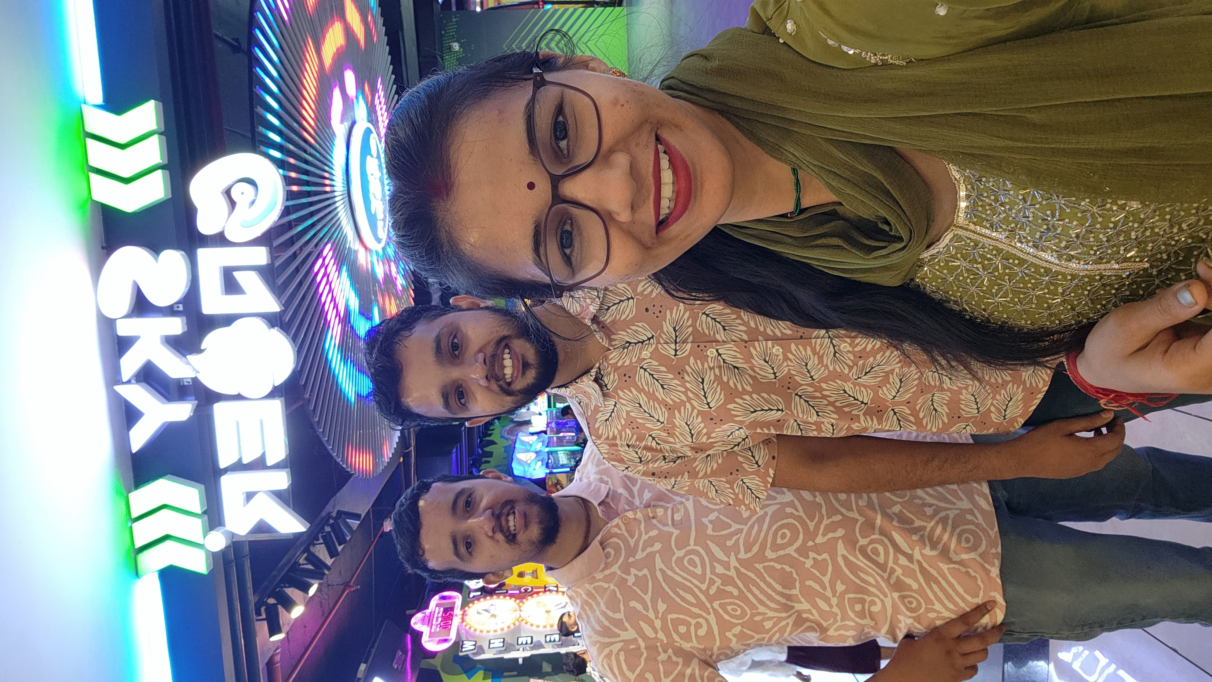 Friends smiling together beneath colorful arcade lights