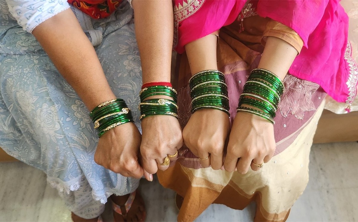 Three wrists wearing rows of green traditional bangles